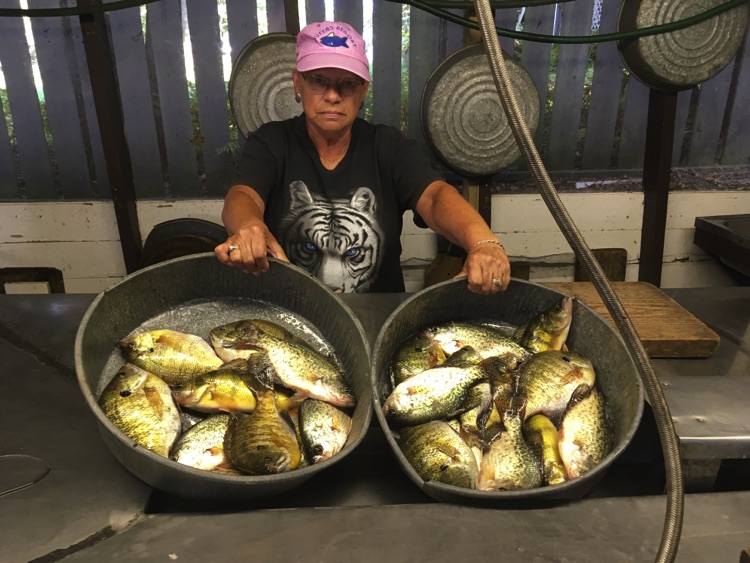 A lady standing in the fish house, showing off a pan of fish she caught on Lake Prairie.