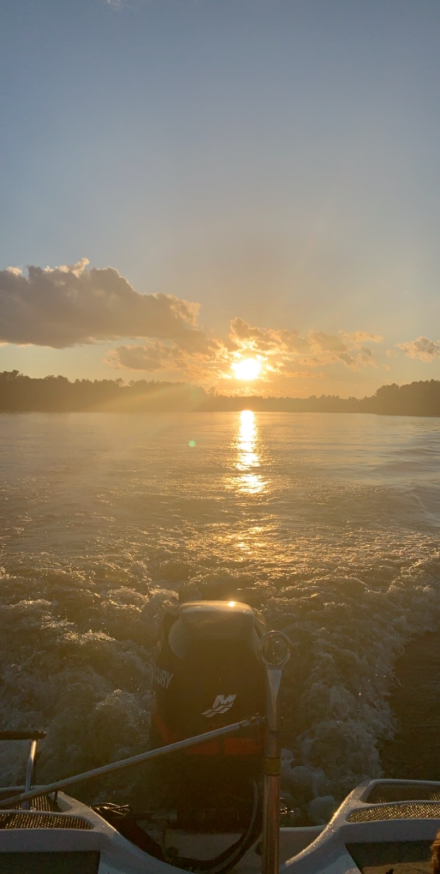 Golden sunrise over the calm lake at Outers Resort, viewed from a moving boat with the outboard motor and wake in the foreground.